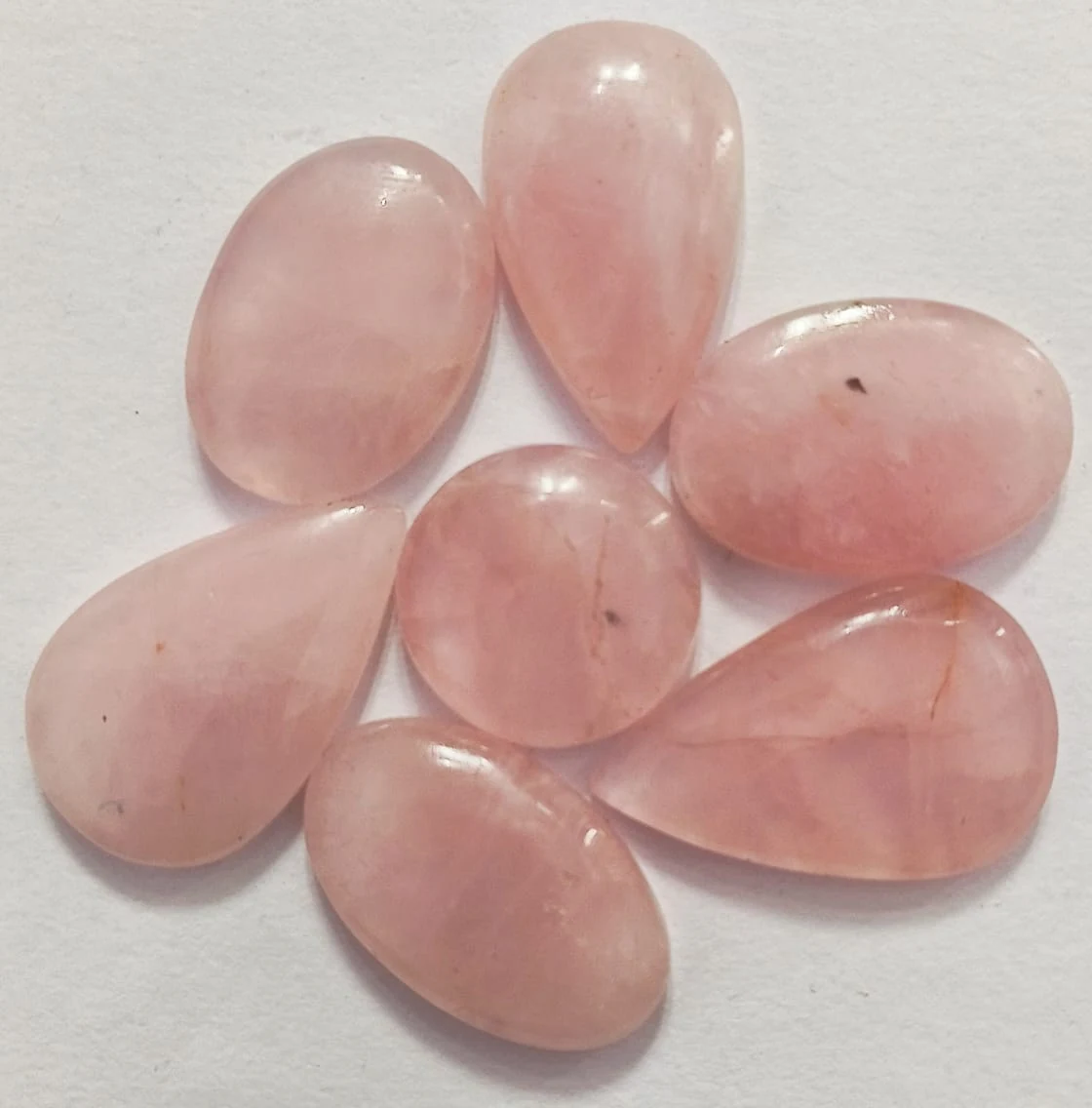 Rose Quartz cabochons arranged on a light polished surface